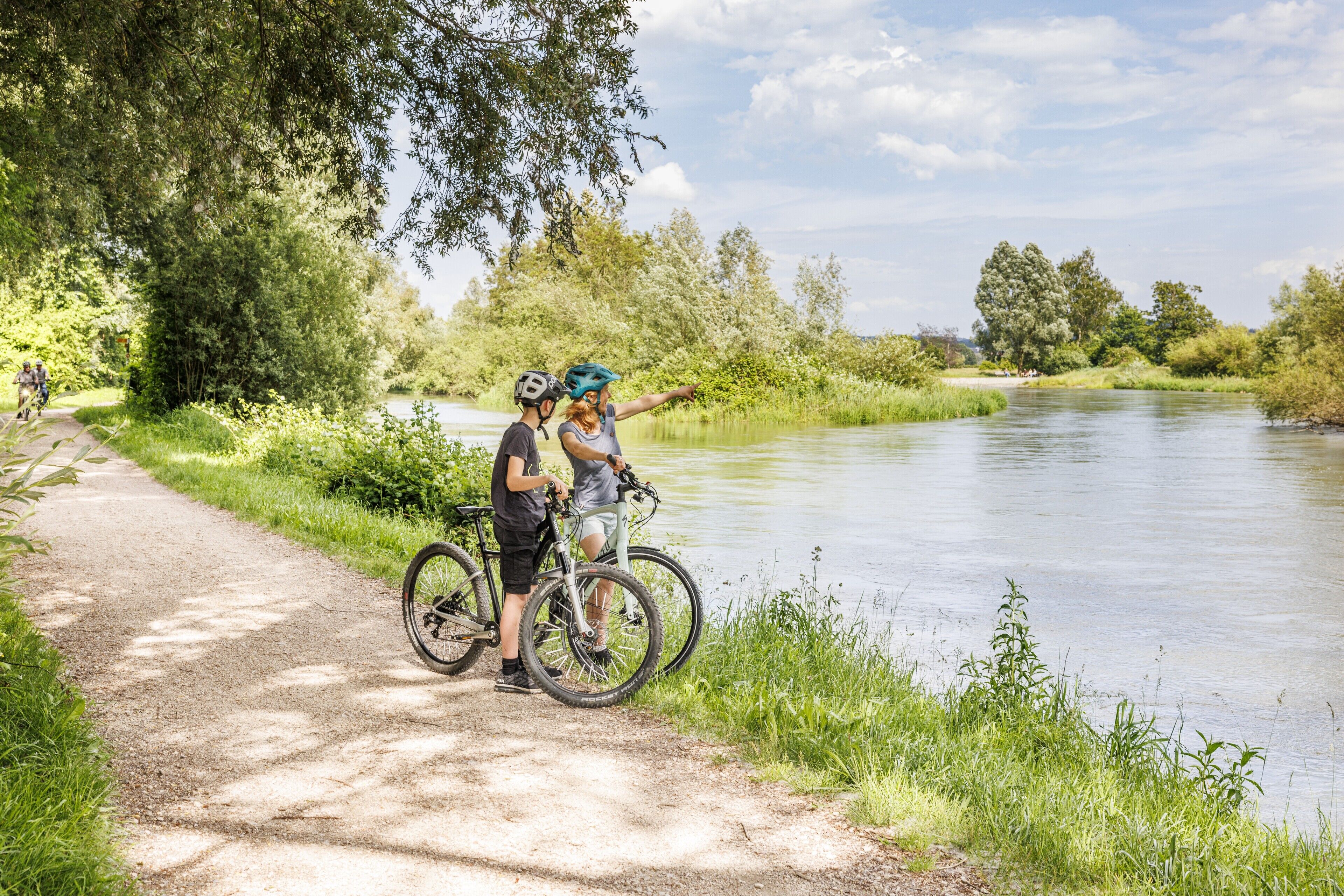 A paved path beside a river with cyclists and a person pointing towards the water.