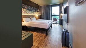 A hotel room with a bed, a desk, a chair, a TV, and a window with curtains. - Ibis Styles Singen (Singen)