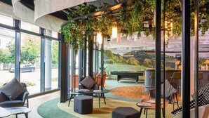 A modern indoor space with a pool table, comfortable seating, and a view of a green landscape through large windows. - Ibis Styles Singen (Singen)