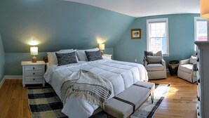 A bedroom with a bed, bedside tables, a chair, a bench, and a window. - Luxury living, quick walk to town. King bed. (Eastport)
