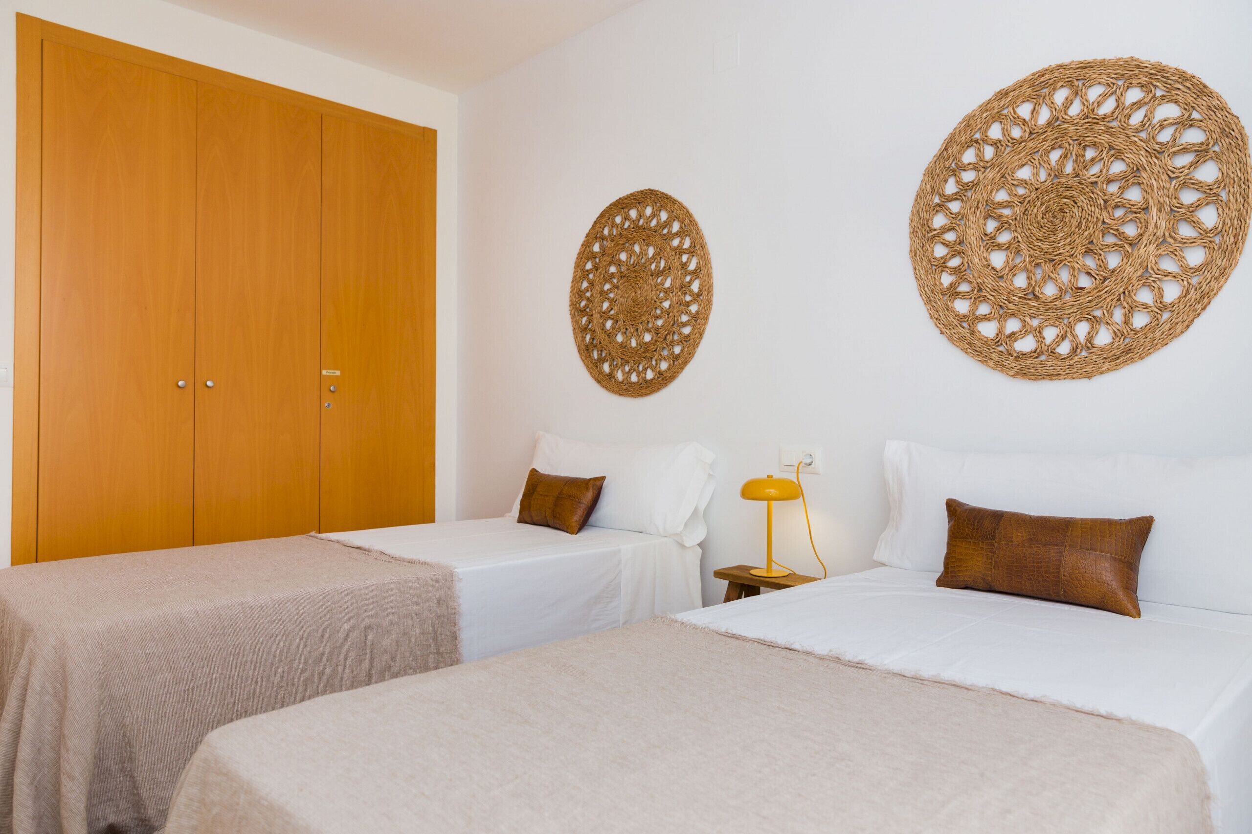 A hotel room with two single beds, a wooden wardrobe, and two wall-mounted decorative items.
