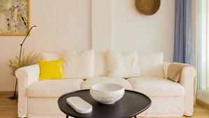 Un sofá blanco con un cojín amarillo, una mesa negra con un cuenco blanco y una lámpara de pie.