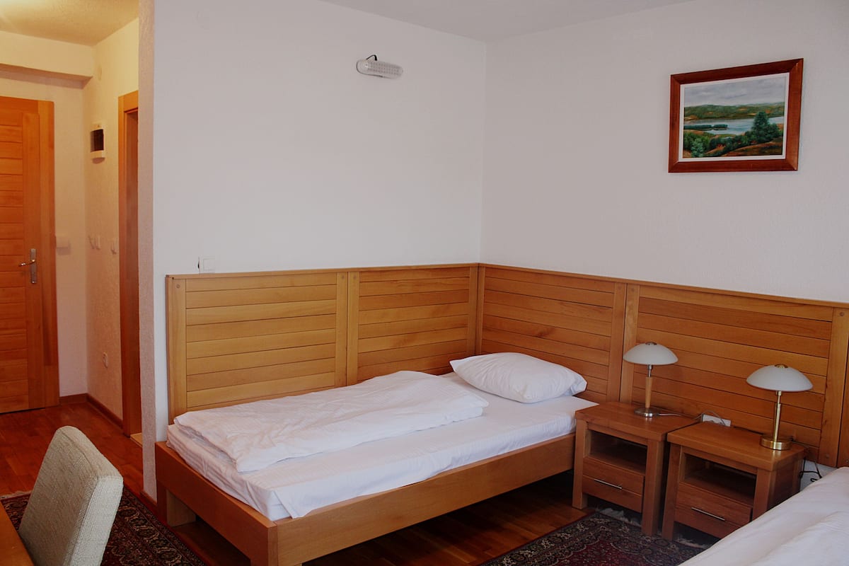 A neatly made bed with a wooden headboard, two bedside tables with lamps, and a framed landscape painting on the wall.