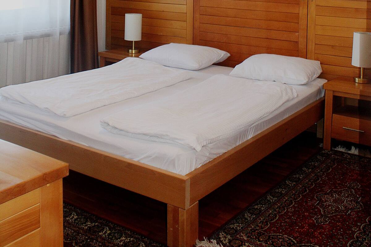 A double bed with wooden headboard, two bedside tables with lamps, a painting on the wall, and a window with curtains.