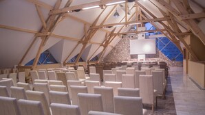 An indoor space with a high, sloped ceiling supported by wooden beams, arranged seating, and a stone wall. - Hotel Borovi Sjenica (Sjenica)