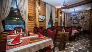 A restaurant with wooden walls, stone accents, and red upholstered chairs. Tables are set with white tablecloths and red napkins. - Hotel Borovi Sjenica (Sjenica)