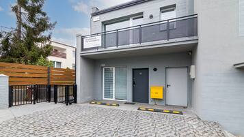 A modern apartment building with a grey facade, a balcony, and a gated entrance.