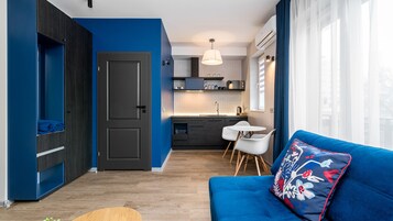 A modern apartment with a blue accent wall, a kitchenette, a dining area, and a living room with a blue sofa and a decorative pillow.