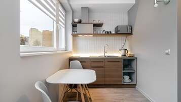 A compact kitchen with a white table and chairs, wooden cabinets, and a window overlooking a cityscape.