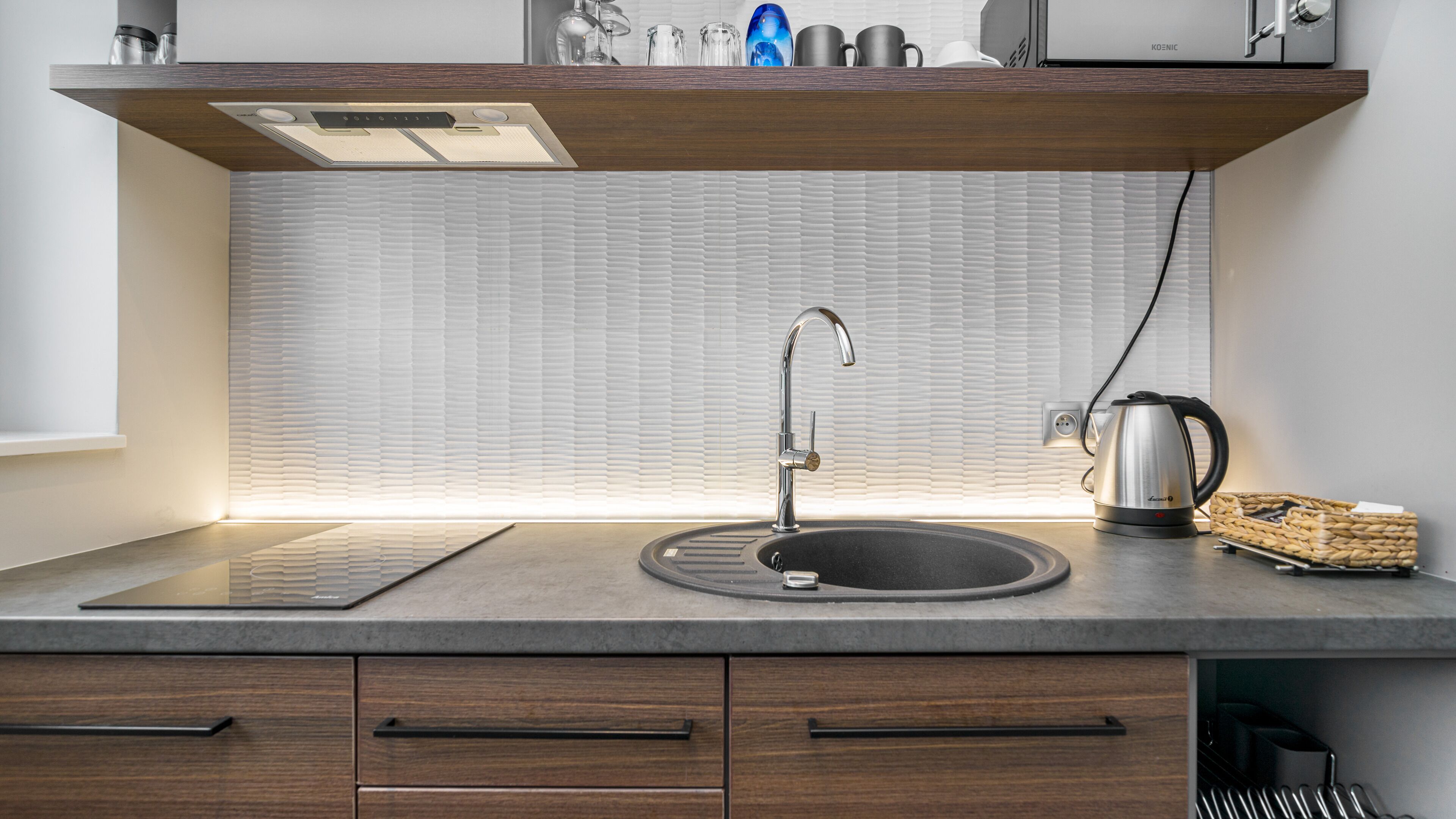A modern kitchen with a built-in sink, a kettle, and a wooden countertop.
