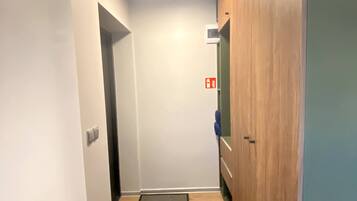 Un pasillo estrecho con una puerta de madera, un felpudo pequeño en la entrada y una lámpara en el techo.