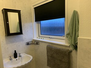 A bathroom with a sink, mirror, window with a black blind, and a towel rack.