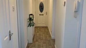 Un pasillo con paredes blancas, suelo de madera y una puerta con panel de vidrio y diseño floral rojo.