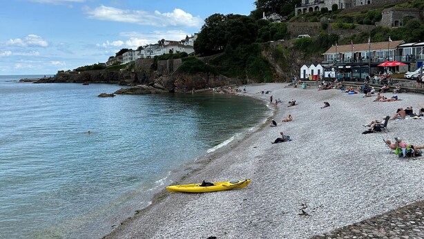 A pebble beach with kayaks and a historic building in the background.