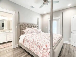 A bedroom with a four-poster bed, a large mirror, and a vanity with a sink.
