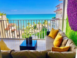 Ein Balkon mit Blick auf das Meer, eine Couch mit gelben Kissen und eine Zierwand.