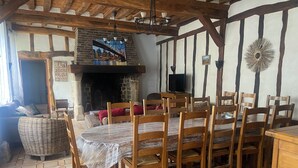 A dining area with a large wooden table and chairs, a stone fireplace, and a view of the city skyline through a window.