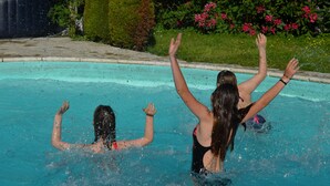 A swimming pool with two people in the water, surrounded by greenery and flowers.