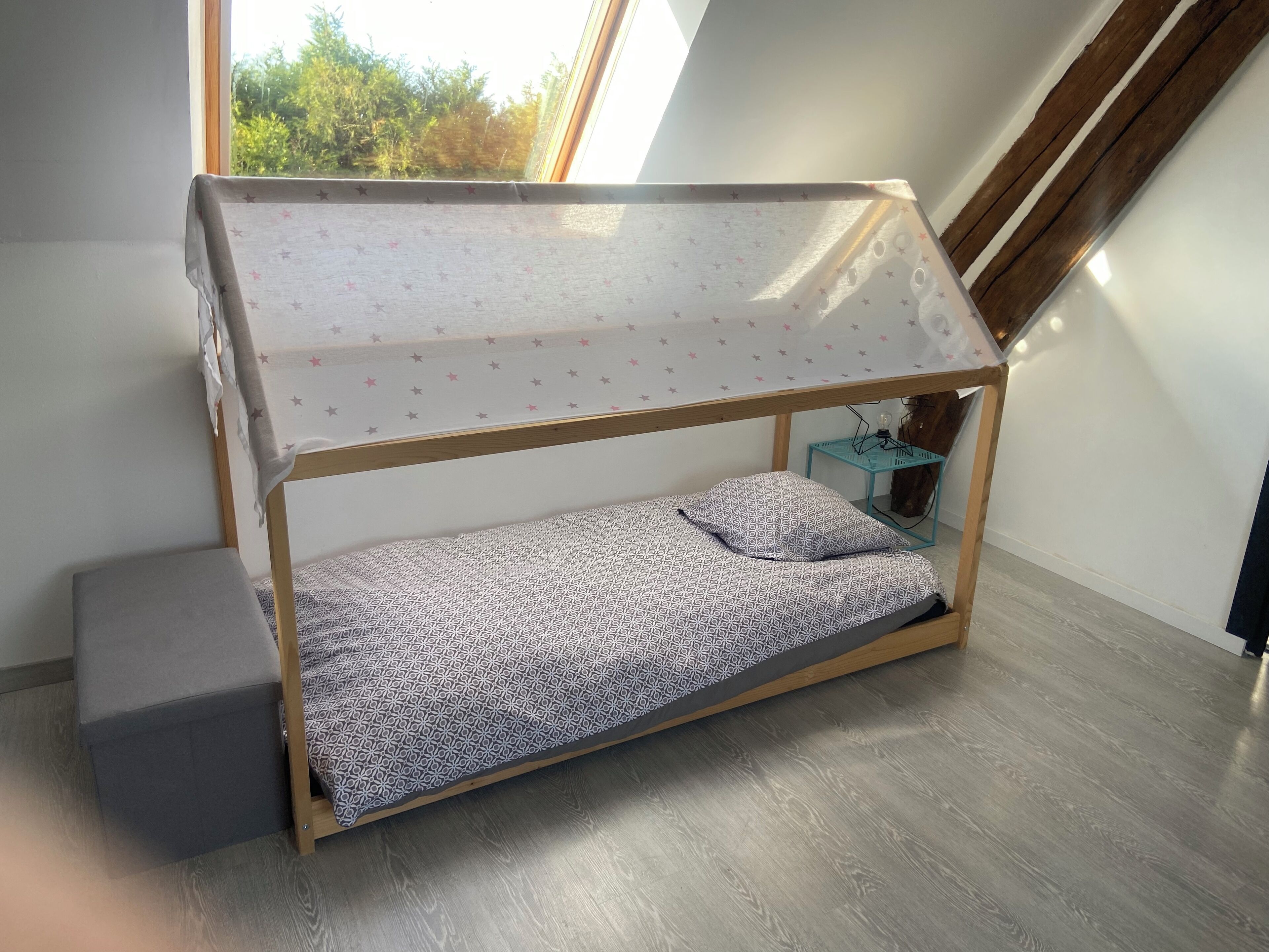 Una cama litera con dosel estampado de estrellas, una mesita de noche pequeña y vistas a zonas verdes al exterior.