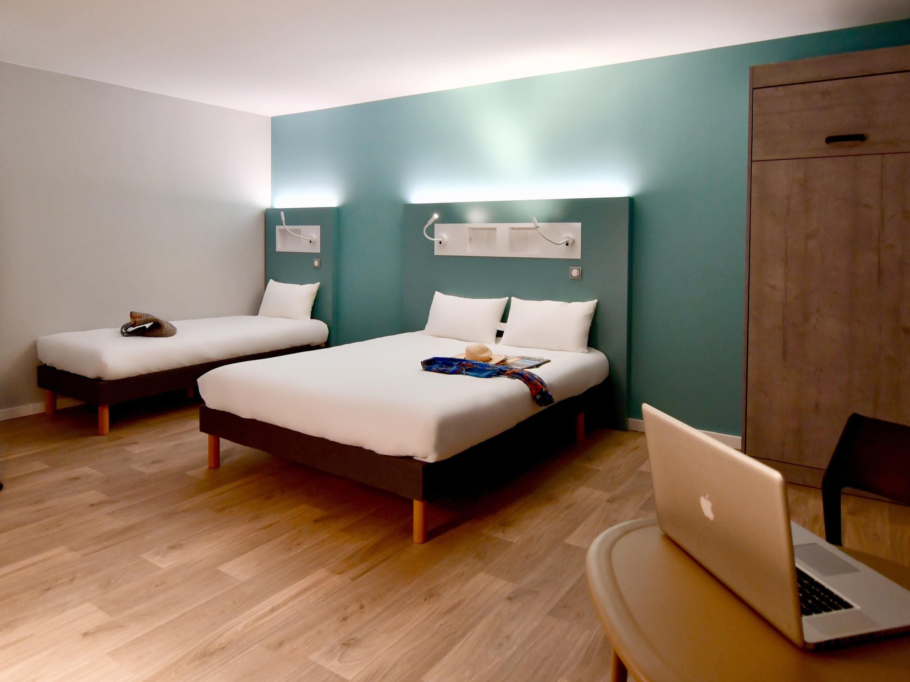 Una habitación de hotel con dos camas individuales, un escritorio con una laptop y un armario.