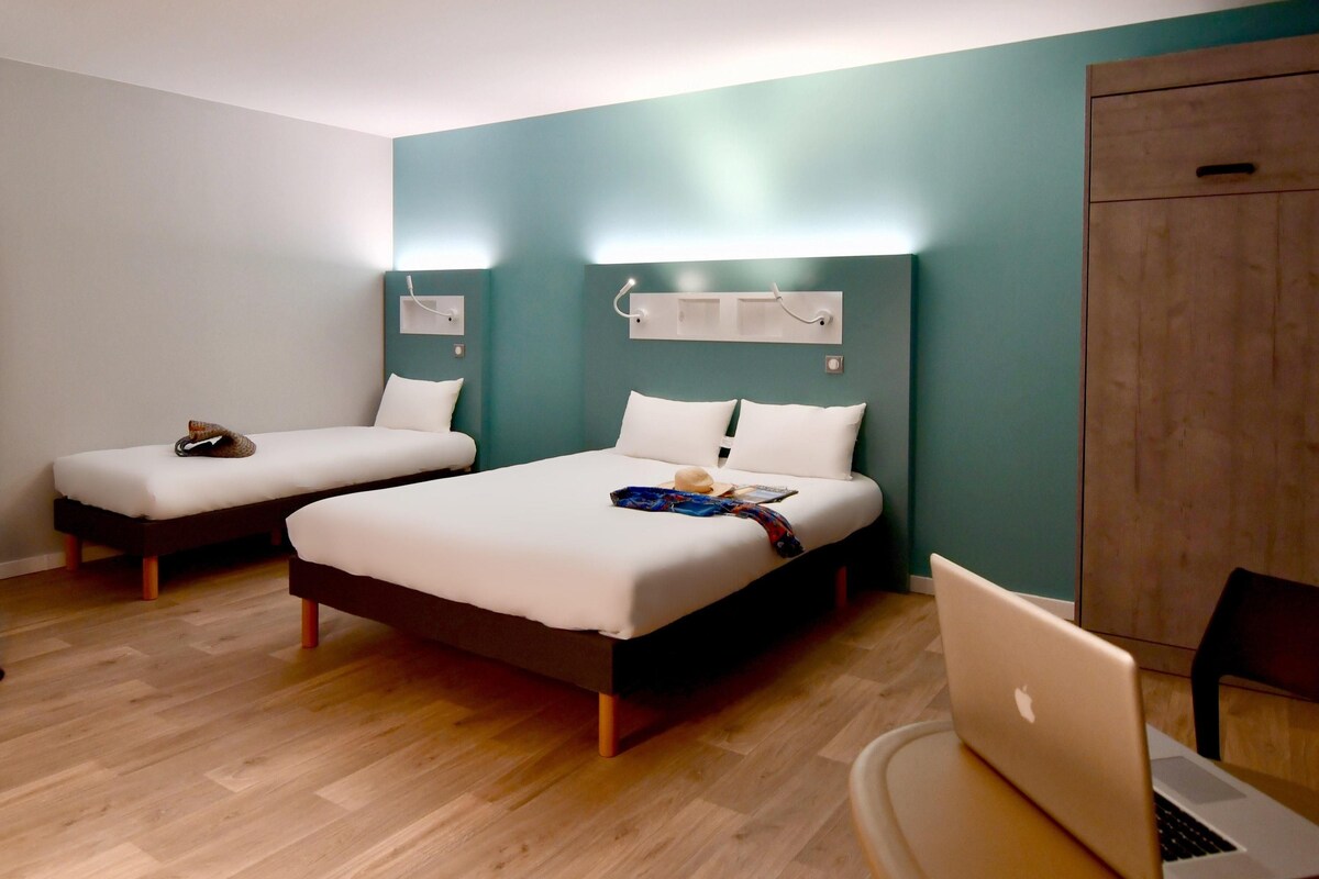 A hotel room with two single beds, a desk with a laptop, and a wardrobe.