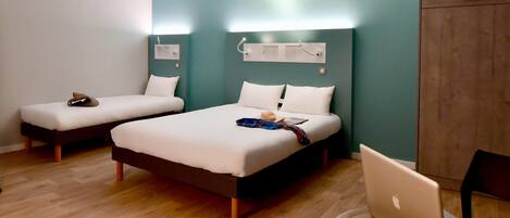 A hotel room with two single beds, a desk with a laptop, and a wardrobe.