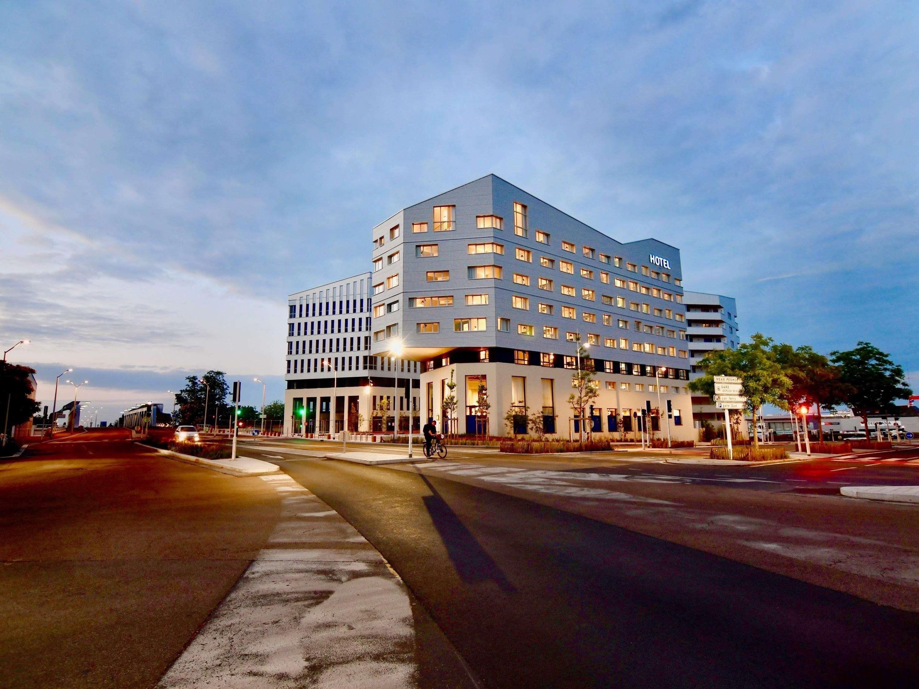 A multi-story hotel with a modern design, featuring a prominent entrance and a large parking area.
