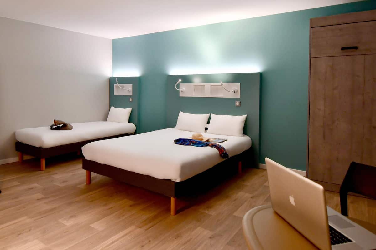 Une chambre d’hôtel avec deux lits simples, un bureau avec un ordinateur portable et une armoire.