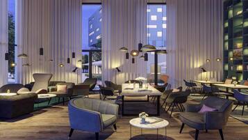 A modern lounge area with a large window, multiple seating options, and a bookshelf.