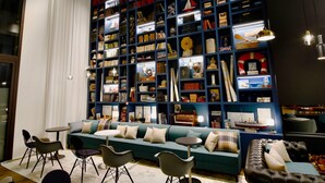 A cozy reading area with a large bookshelf filled with books and decorative items, a teal sofa, and modern chairs. - Ibis Budget Saint Nazaire Centre Gare (Saint-Nazaire)