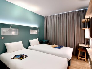 A hotel room with two beds, a desk, a laptop, and a suitcase. - Ibis Budget Saint Nazaire Centre Gare (Saint-Nazaire)