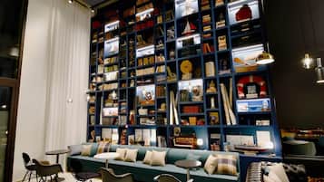 Ein gemütlicher Lesebereich mit einer großen Bücherwand, gefüllt mit Büchern und Dekorationsgegenständen, einem blaugrünen Sofa und modernen Sesseln.