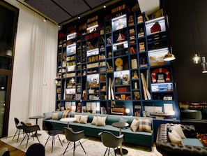A cozy reading area with a large bookshelf filled with books and decorative items, a teal sofa, and modern chairs. - Ibis Budget Saint Nazaire Centre Gare (Saint-Nazaire)