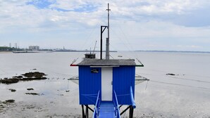 A blue pier leading to a small blue building with a white base, overlooking a calm body of water with distant buildings. - Ibis Budget Saint Nazaire Centre Gare (Saint-Nazaire)