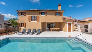 A two-story house with a swimming pool, sun loungers, and a barbecue area.