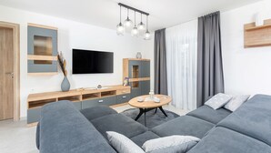 A modern living room with grey sofas, a wooden TV stand, a flat-screen TV, and a round coffee table.