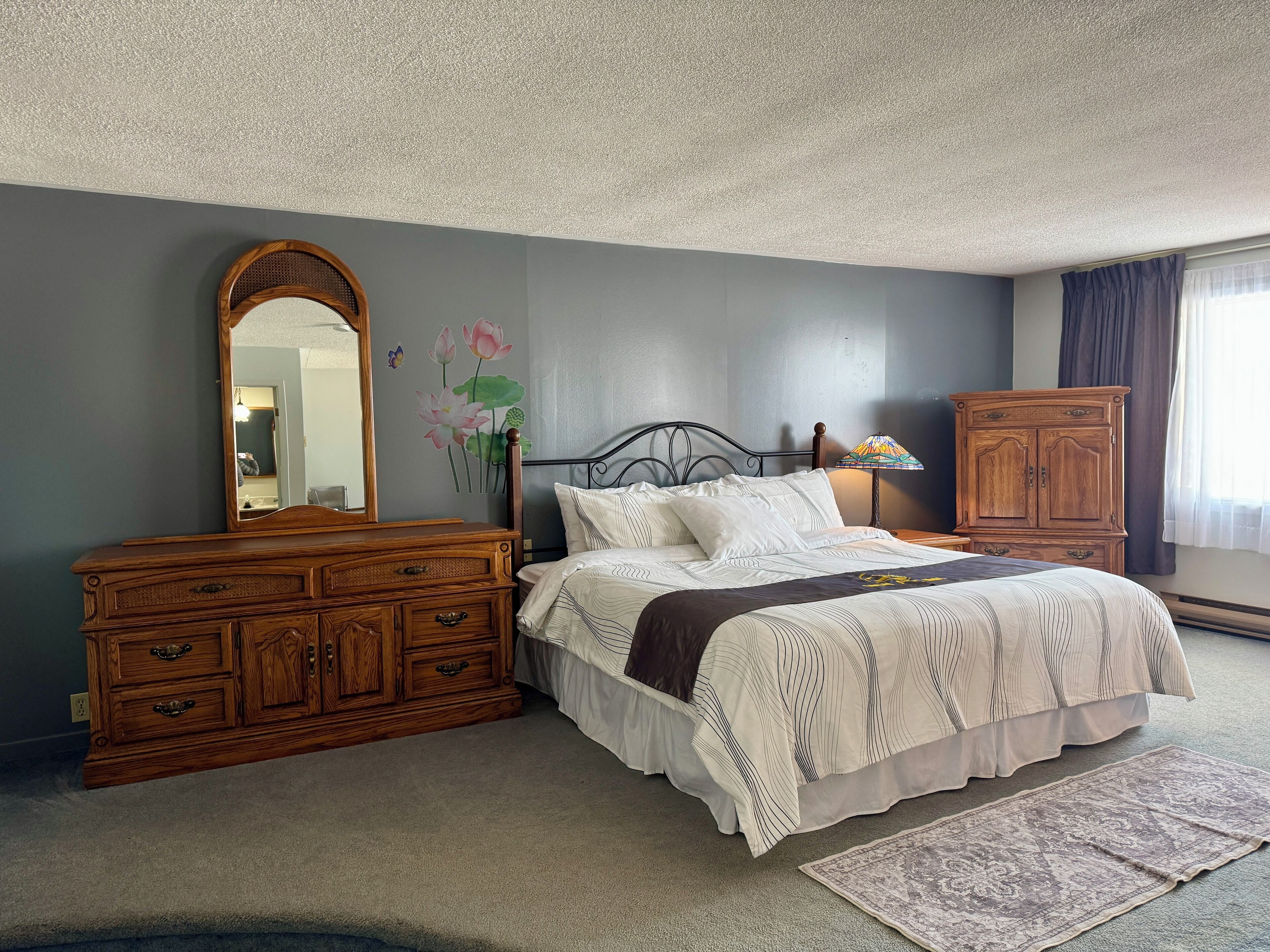 A bedroom with a bed, dresser, mirror, and a wall with a floral mural.