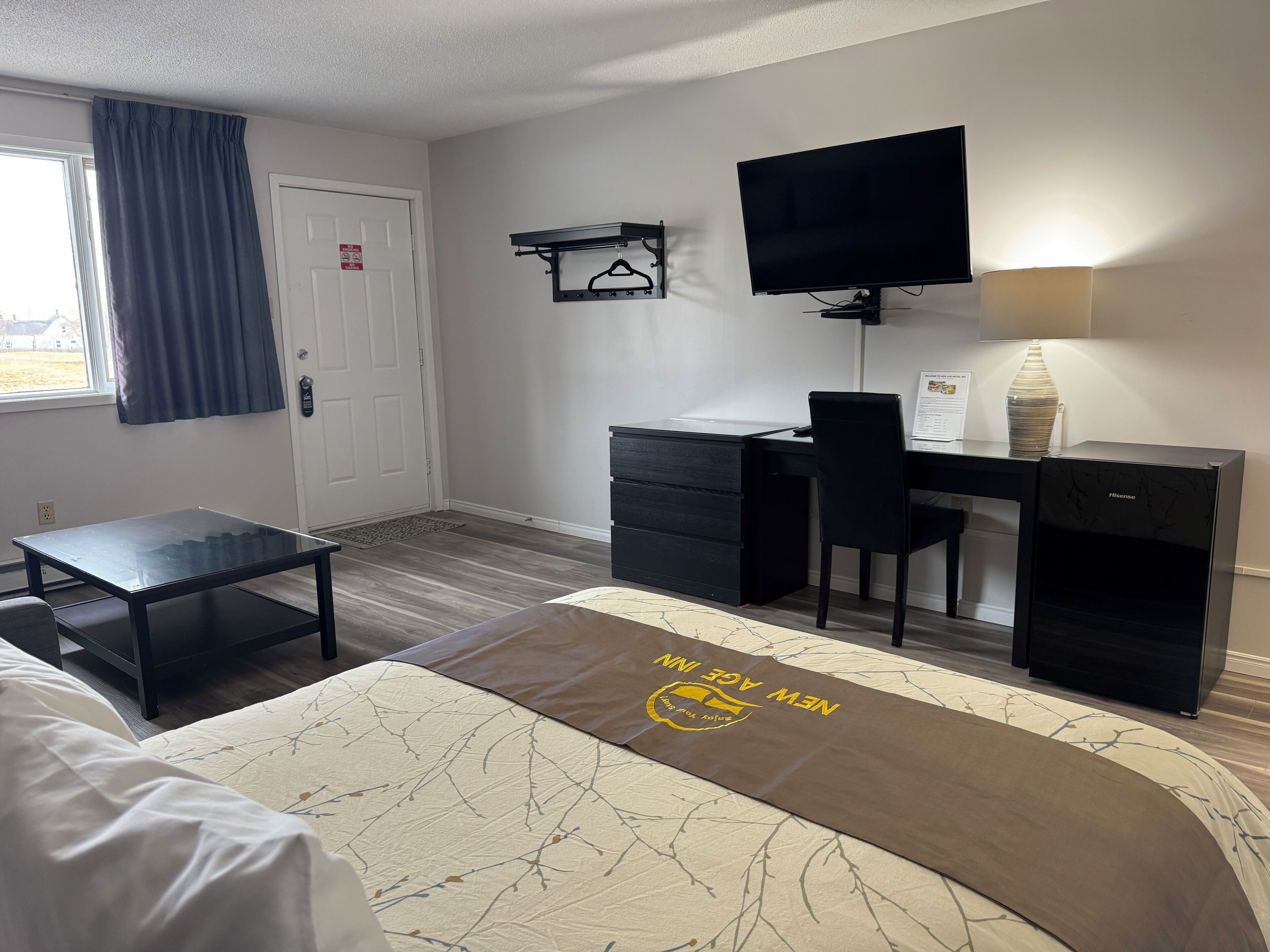 A hotel room with a bed, a desk, a chair, a television, and a window with curtains.