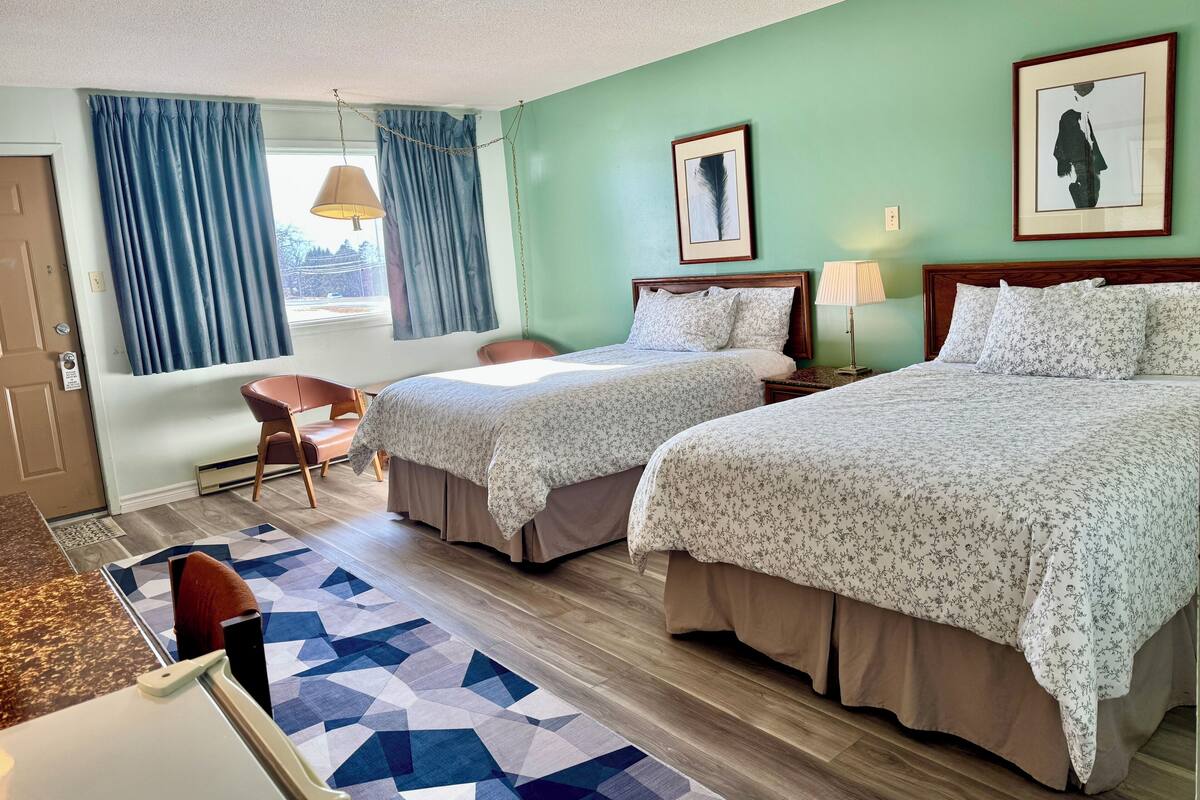 A hotel room with two beds, a desk, a chair, and a window with curtains.