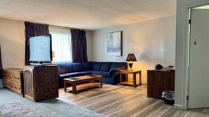 Una sala de estar con un sofá, una mesa de centro, televisor y una lámpara.