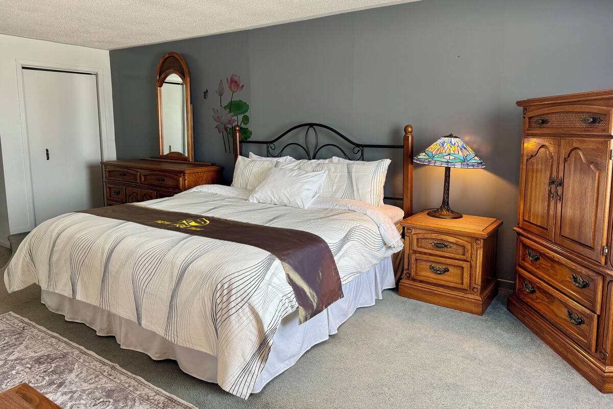 A bedroom with a bed, a nightstand, a dresser, a mirror, and a wall with a floral decoration.
