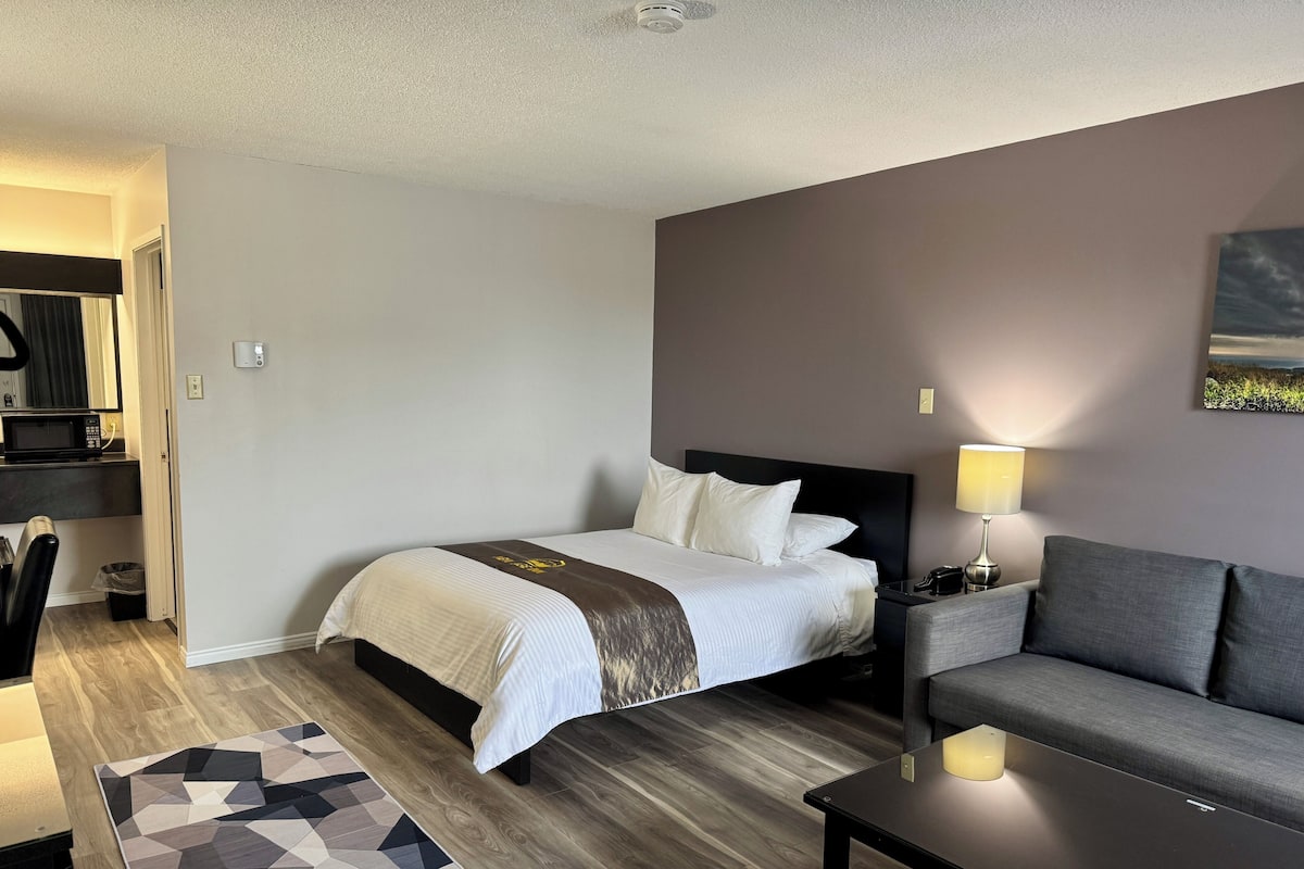 A hotel room with a bed, a sofa, a lamp, and a painting on the wall.