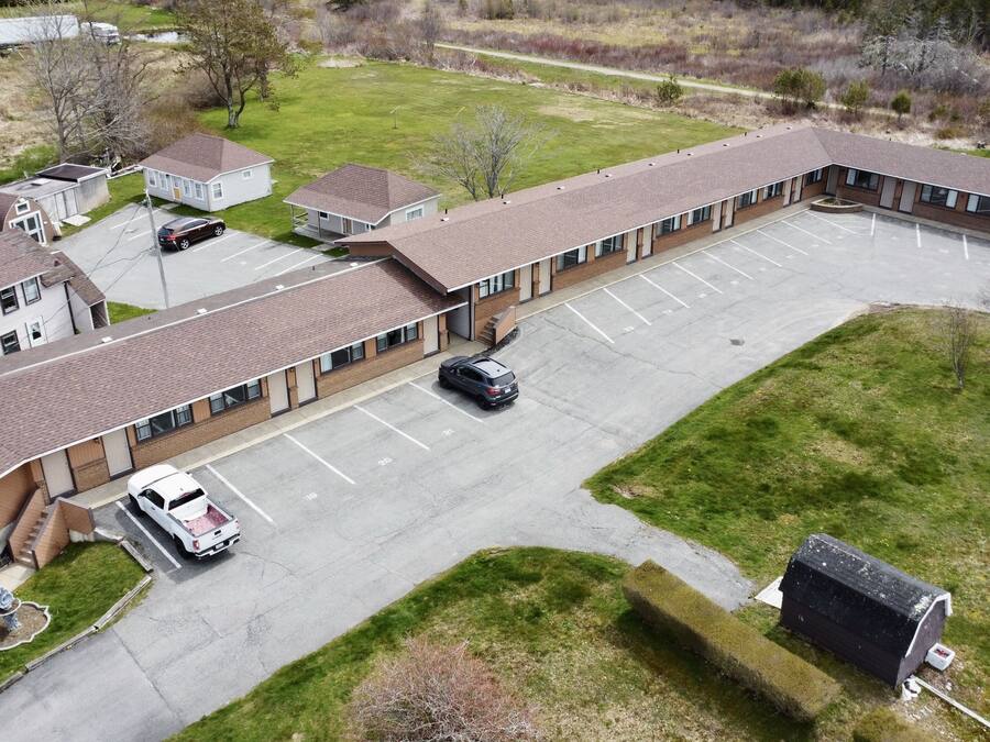 Ein Motel mit einem zentralen Parkplatz, separaten Einheiten mit angebauten Garagen und einem kleinen Außenbereich mit Müllbehälter.