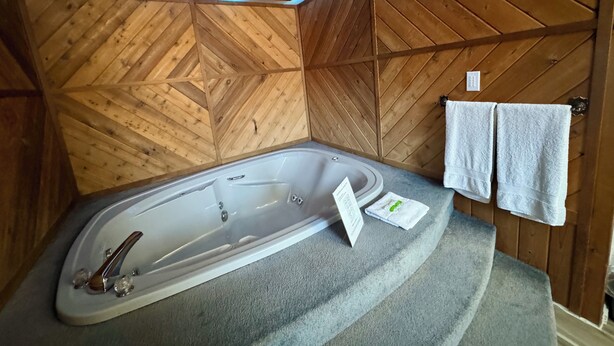 Un baño de estilo cabaña de madera con una bañera independiente, un perchero con toallas y una pared de madera con un diseño en chevron.