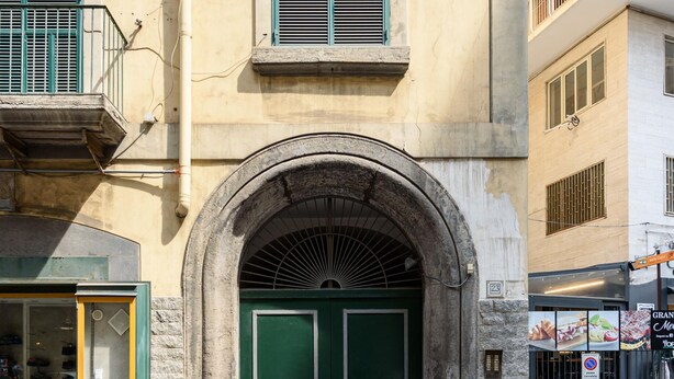 Un edificio con una porta verde a doppio battente, un arco in pietra e un piccolo balcone con ringhiera in metallo.