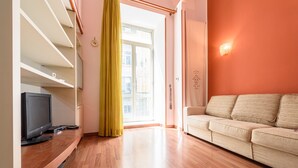 Un soggiorno con televisore su un supporto in legno, un divano beige e una grande finestra con tenda gialla.