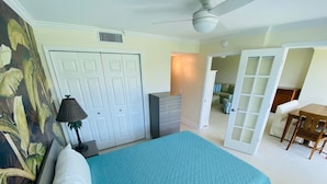 A bedroom with a bed, a dresser, a desk, and a chair. There is a door leading to another room.