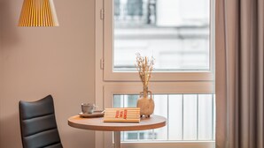 Una habitación de hotel con una cama, una mesa redonda con un jarrón de plantas secas, una silla y una lámpara.