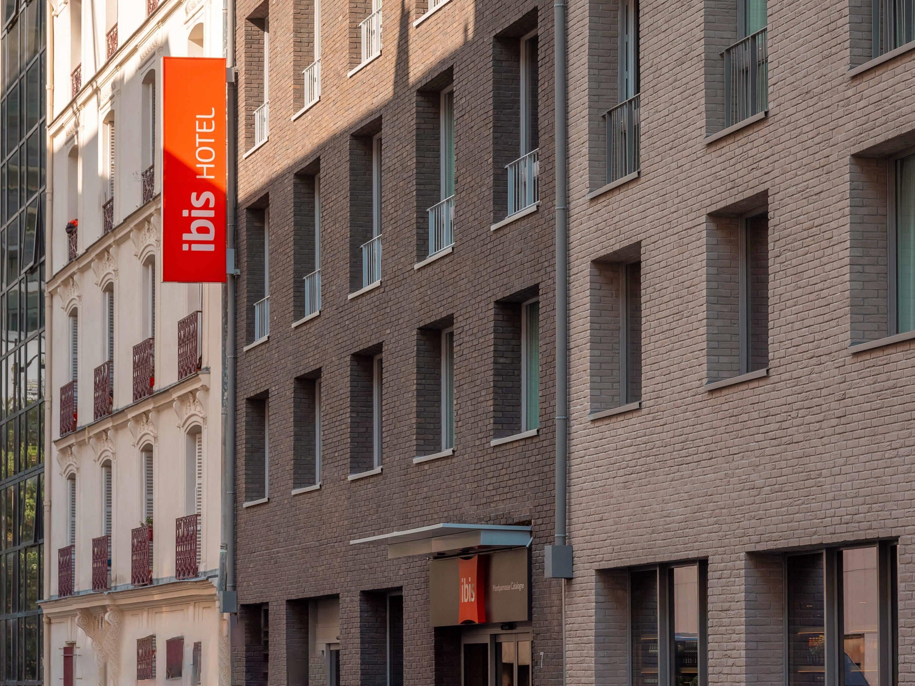 A hotel building with a prominent red sign, multiple windows, and a mix of brick and classical facade elements.