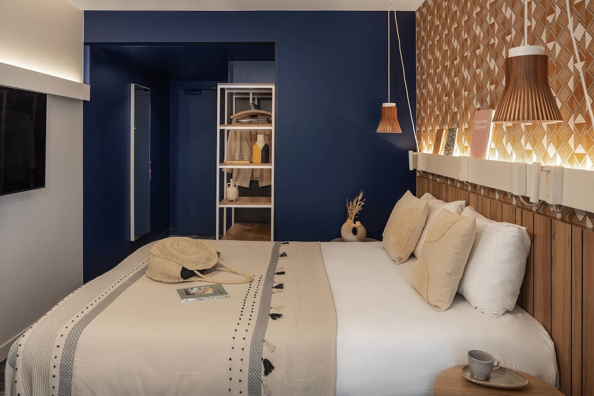 Une chambre moderne avec un grand lit, une table de chevet sur laquelle se trouve une tasse, une armoire et une lampe suspendue.